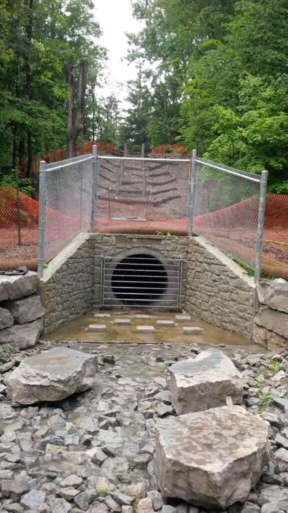 concrete drainage tunnel and headwall surrounded by rocks and a chain link fence